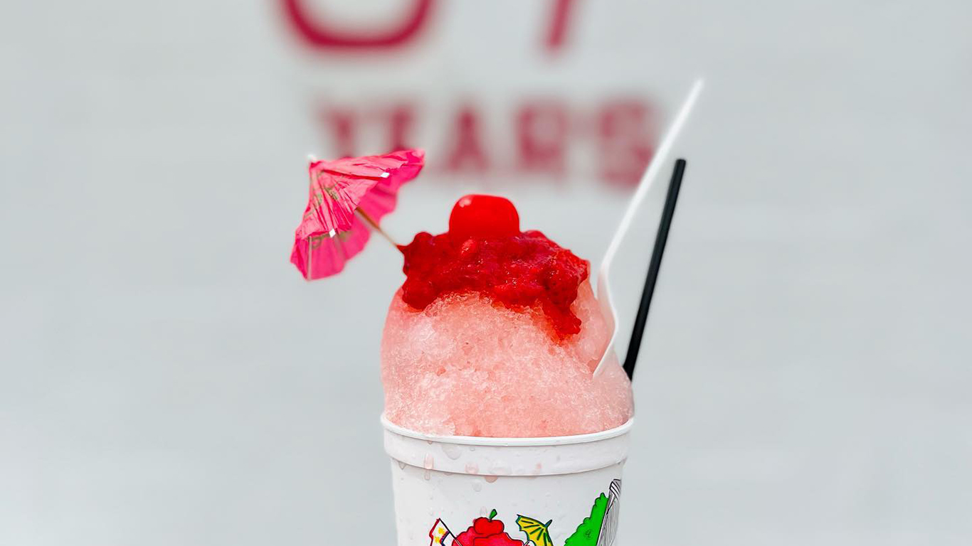 A pink and red snoball fills a cup, and is topped with a small drink umbrella.