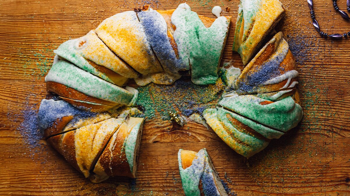A sliced traditional king cake atop a cutting board.