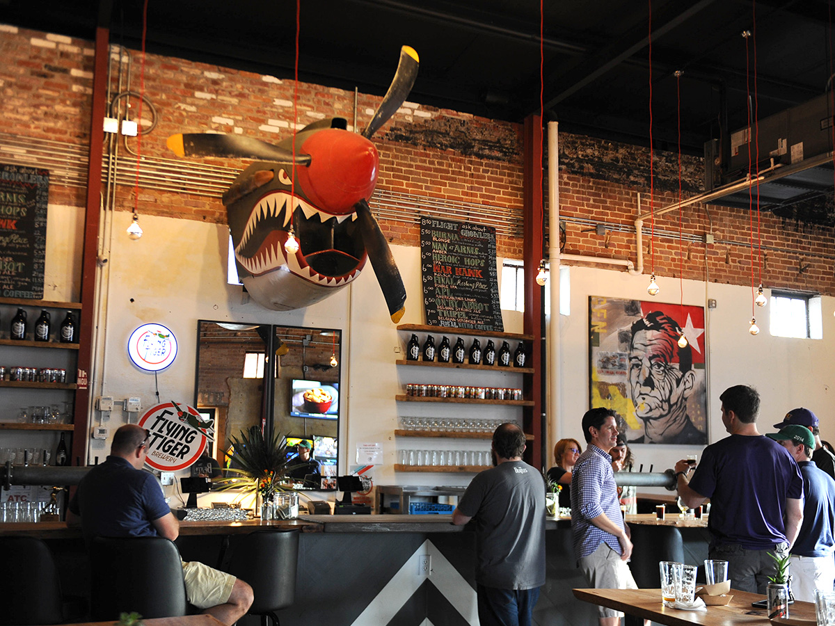 Flying Tiger Brewery Monroe Interior of Flying Tiger Brewery in Monroe, Louisiana, featuring airplane-themed shark sculpture mounted above the bar and customers ordering drinks.