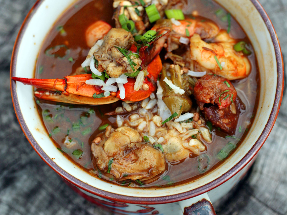 A red bowl piled high with seafood gumbo in a rich, tomato broth, with shrimp, crawfish and other seafood.